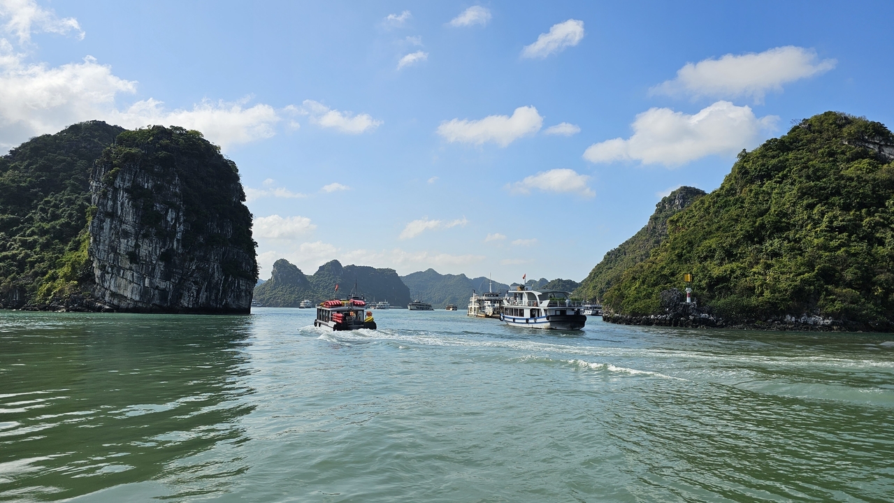 Vue de bateaux et de formations calcaires dans la baie d'Halong sous un ciel bleu dégagé.