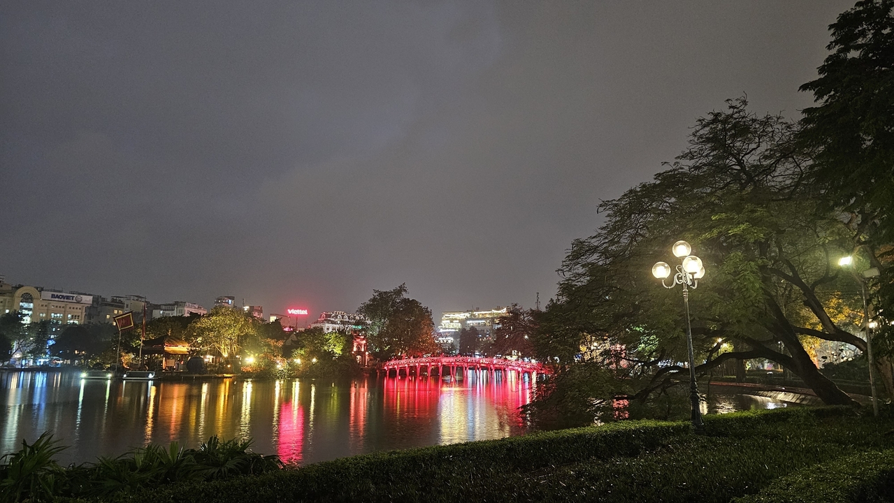 Vue nocturne d'un lac avec un pont éclairé en rouge à Hanoï.