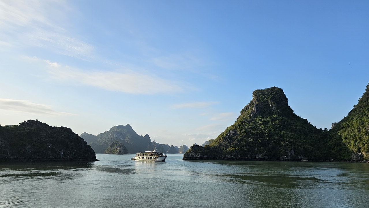 Vue panoramique des karsts calcaires et d'un bateau dans la baie d'Halong sous un ciel bleu.
