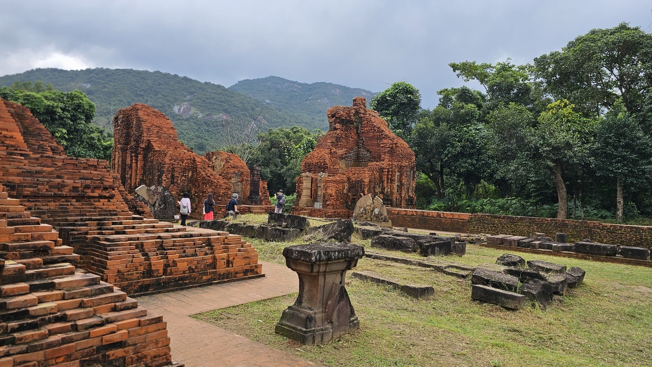 Anciennes ruines de brique entourées de verdure et de montagnes, possiblement le sanctuaire de My Son.