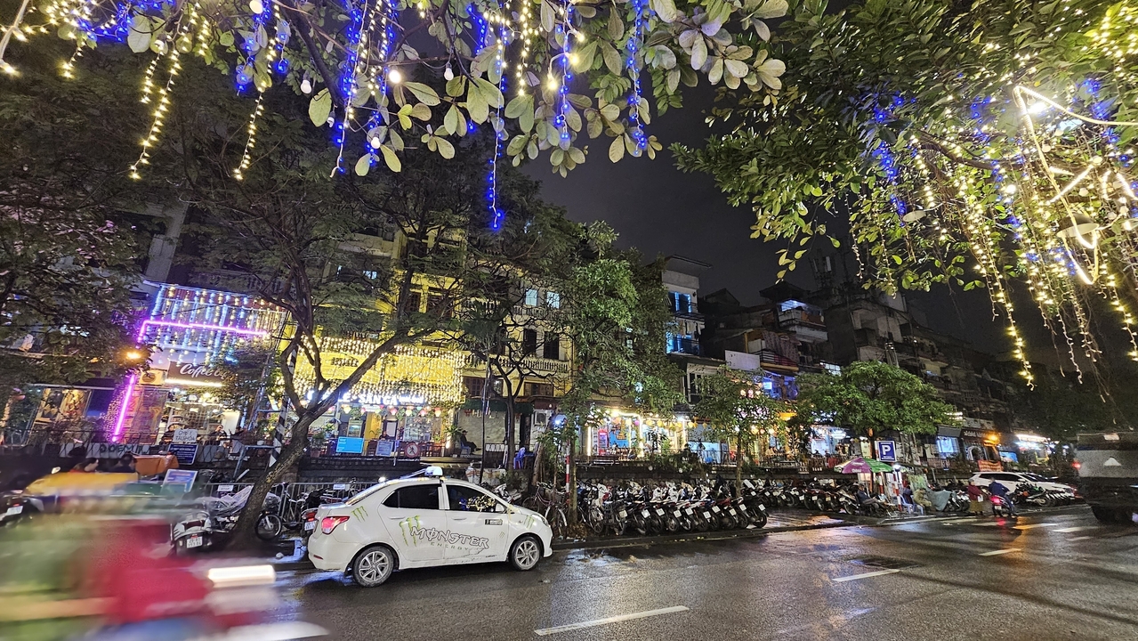 Scène de rue nocturne à Hanoï avec des lumières colorées et un taxi.