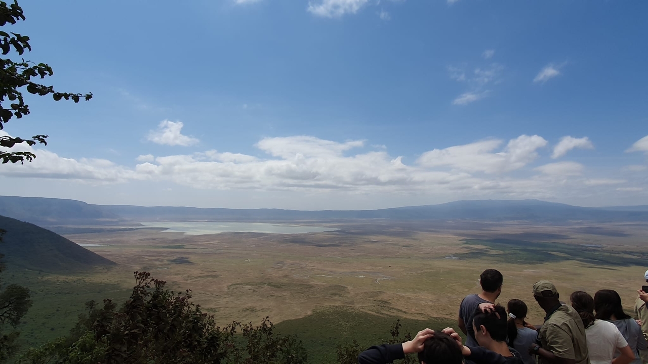 Vue sur une grande prairie et un lac avec des personnes au premier plan.
