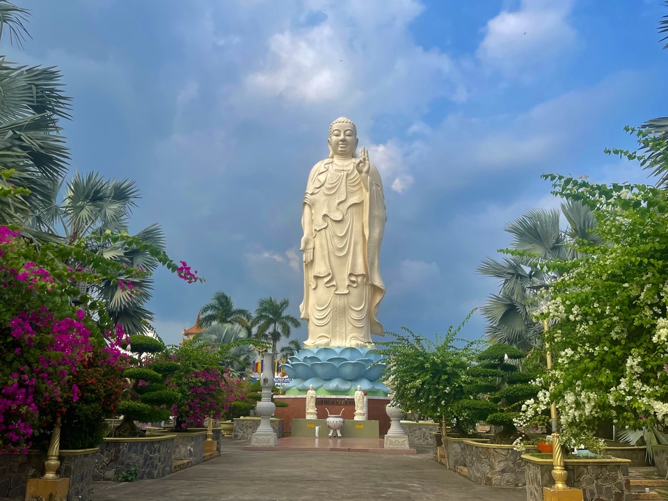 Grande statue de Bouddha extérieure avec des fleurs vibrantes tout autour.