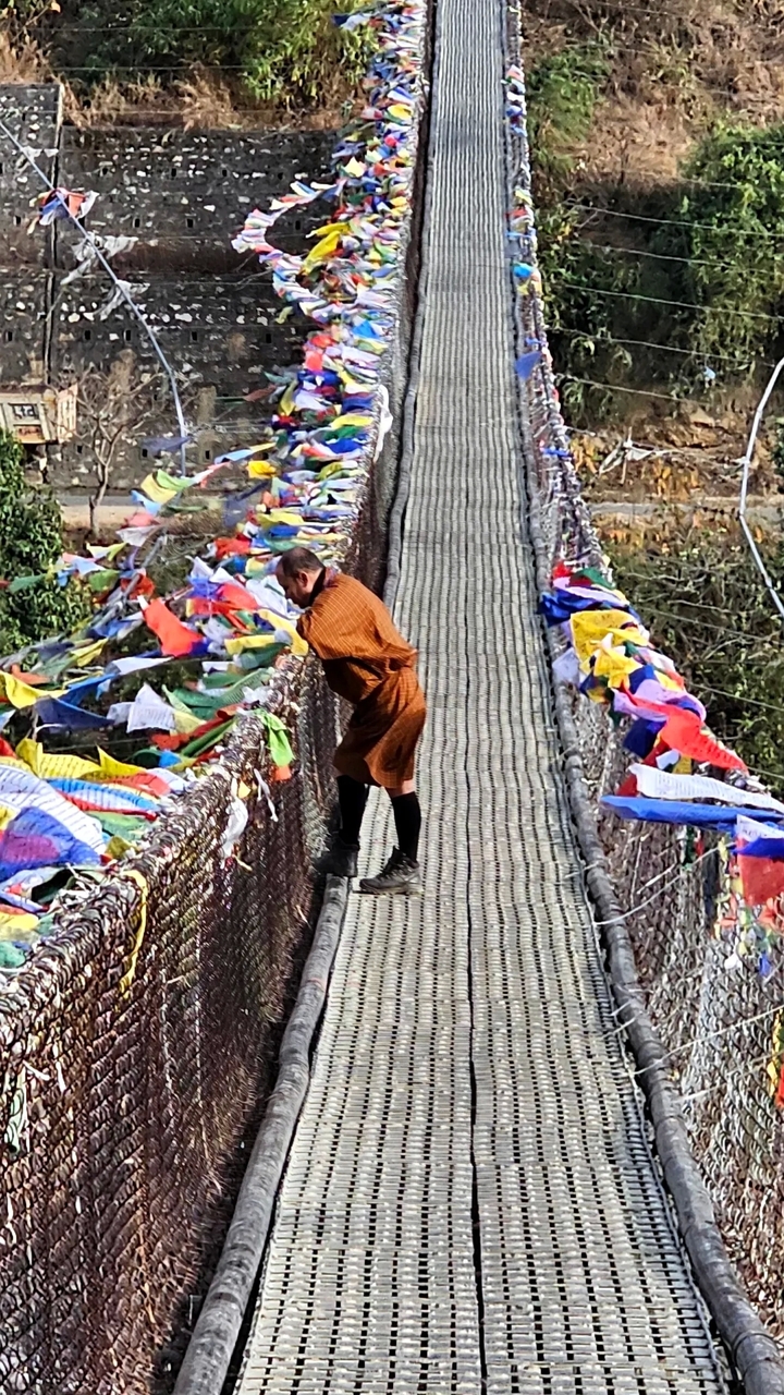 Homme sur un pont avec des drapeaux de prière colorés.
