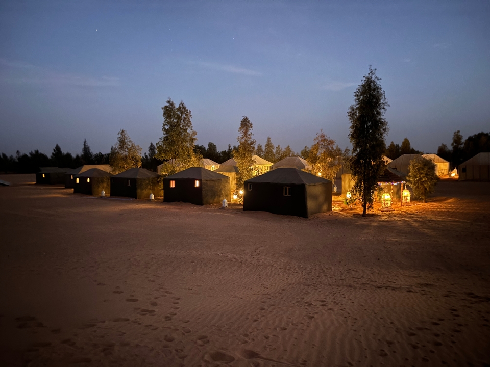 Campement dans le désert avec des tentes éclairées au crépuscule.