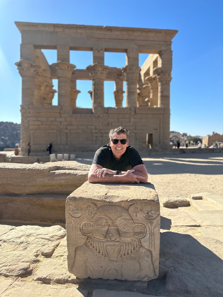 Un homme souriant en posant avec une architecture égyptienne antique en arrière-plan.