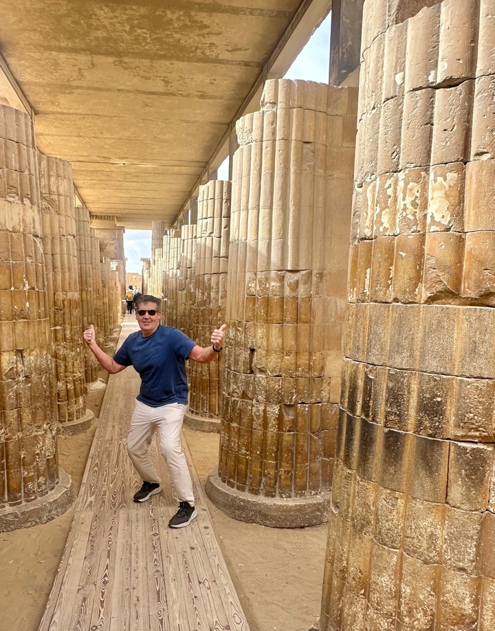 Un homme posant entre des colonnes antiques dans un temple égyptien.