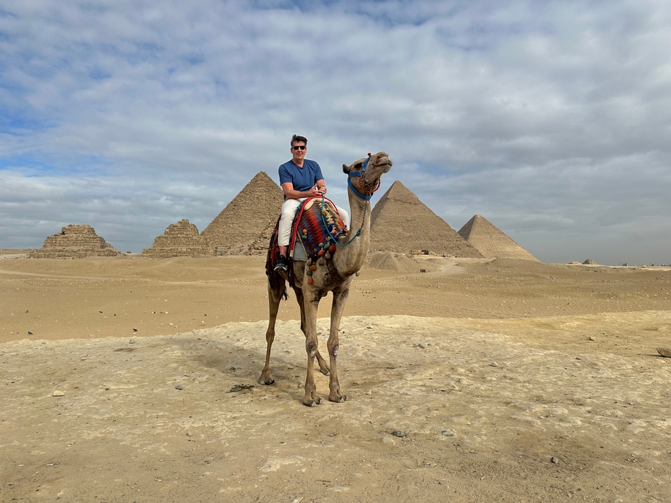 Homme assis sur un chameau avec les pyramides en arrière-plan.