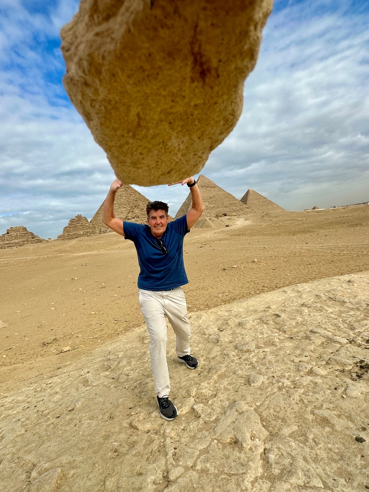 Homme soulevant un poids imaginaire avec des pyramides en arrière-plan.