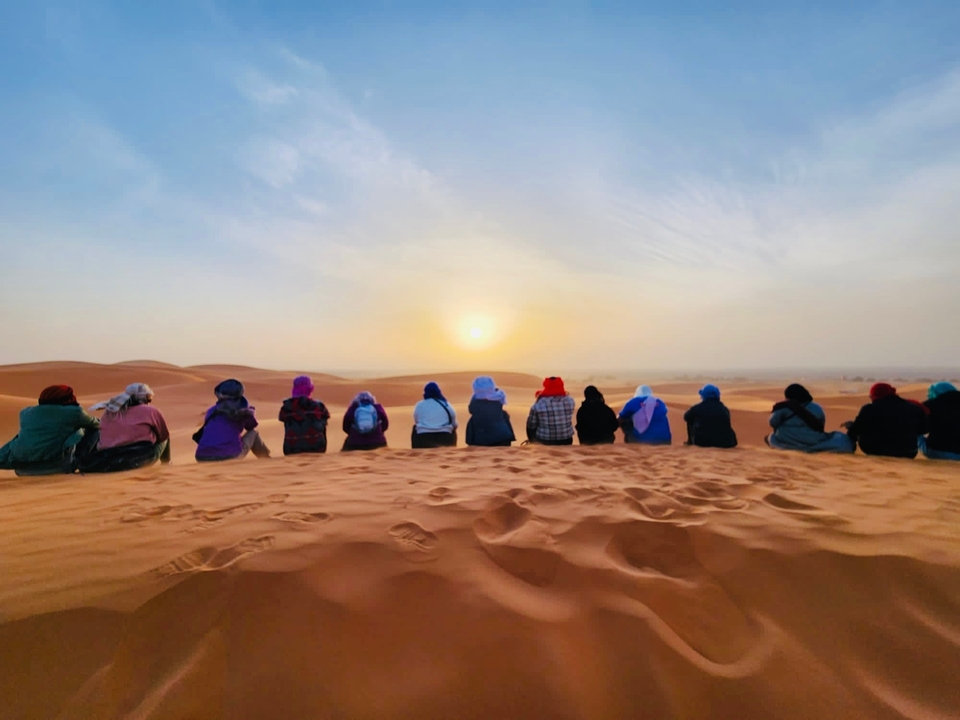 People sitting on a sand dune watching a desert sunset.