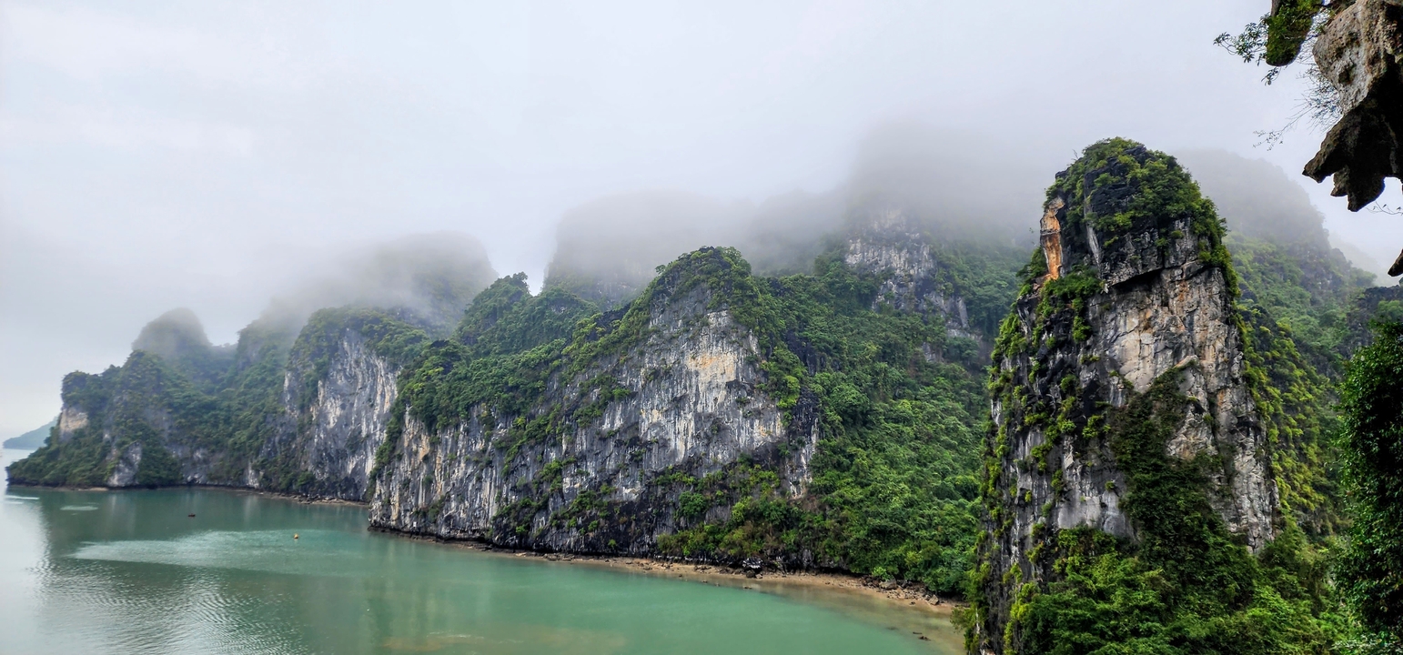 Des karsts calcaires s'élevant de l'eau dans la baie d'Ha Long, enveloppés de brume.