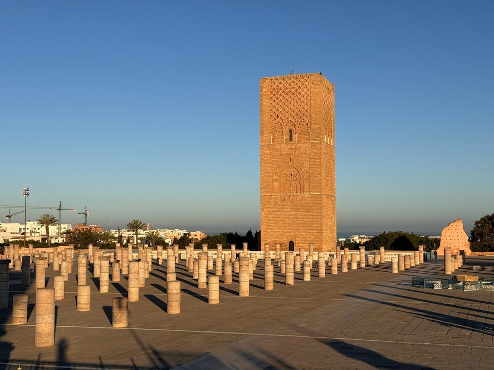 Un minaret de brique élancé et des rangées de piliers sous le ciel bleu.
