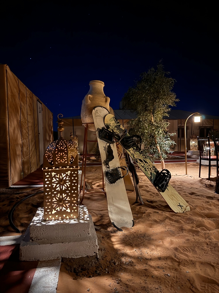 Planches à neige appuyées contre une lanterne décorative dans un complexe touristique du désert la nuit.