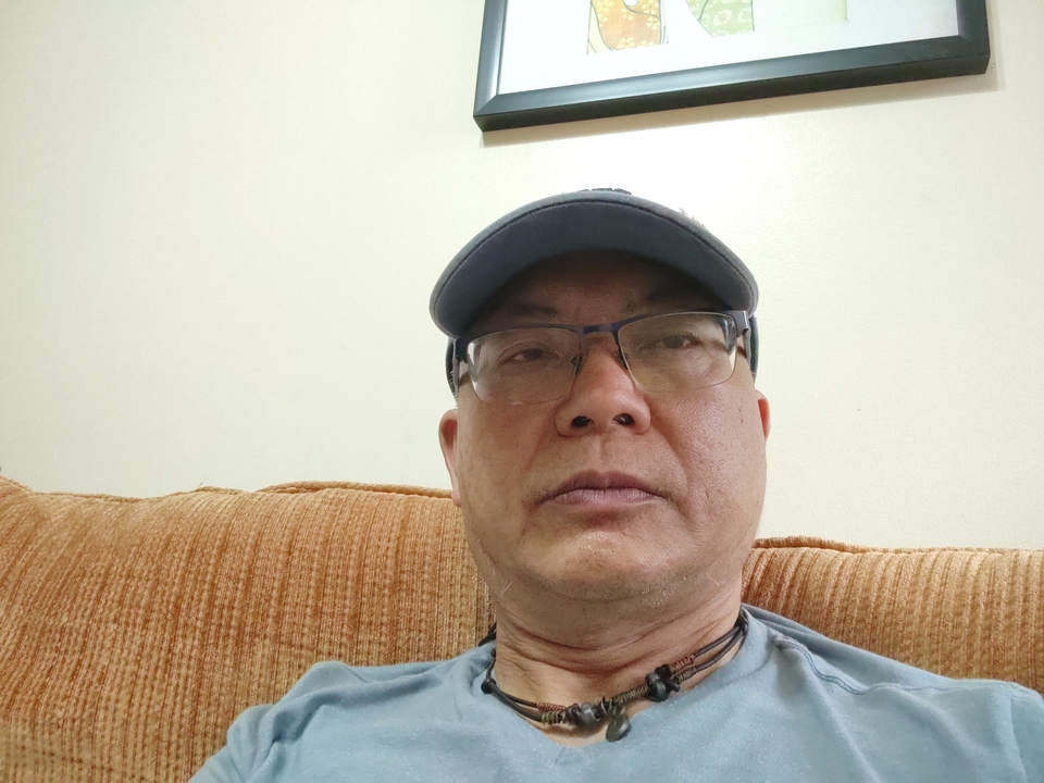 Un homme assis sur un canapé à l'intérieur, regardant directement vers la caméra.