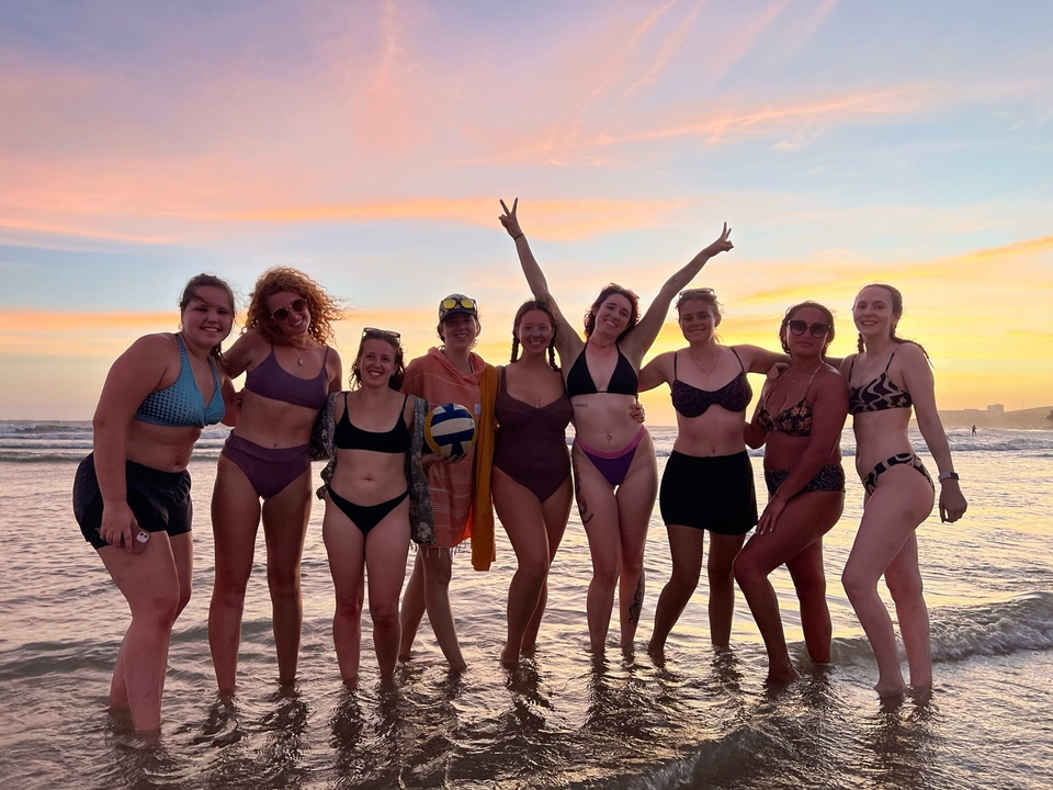 Groupe de personnes en maillots de bain sur une plage au coucher du soleil.