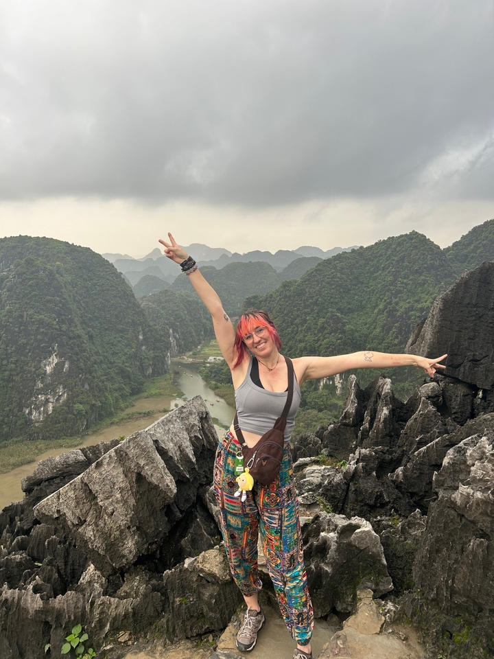 Personne qui pose sur des collines rocheuses avec un paysage pittoresque en arrière-plan.