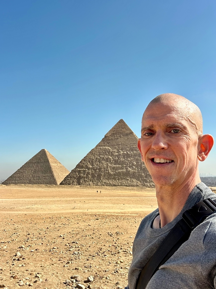 Personne souriante avec deux pyramides en arrière-plan.