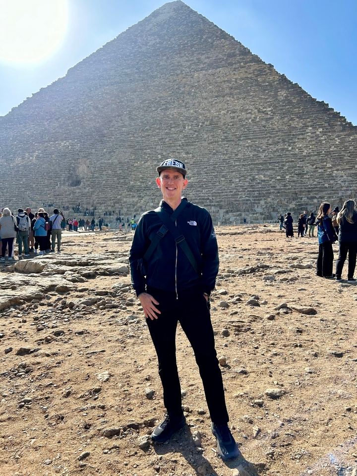 Personne posant devant une pyramide avec des touristes autour.