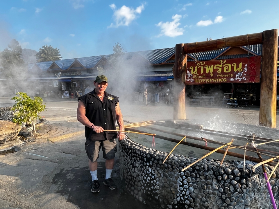 Homme debout près d'une source chaude fumante dans une zone touristique.