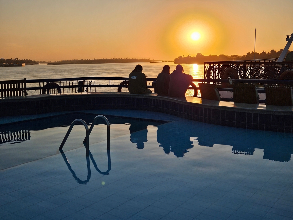 Silhouette de personnes regardant le coucher de soleil sur une rivière depuis un bateau de croisière.