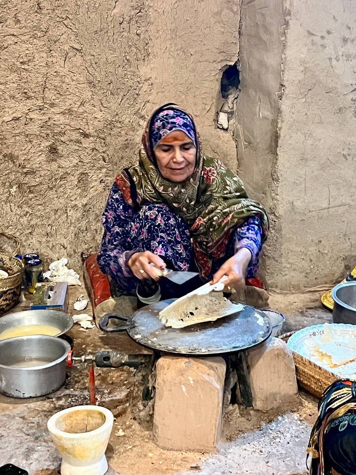 Femme préparant de la nourriture traditionnelle dans un cadre extérieur.