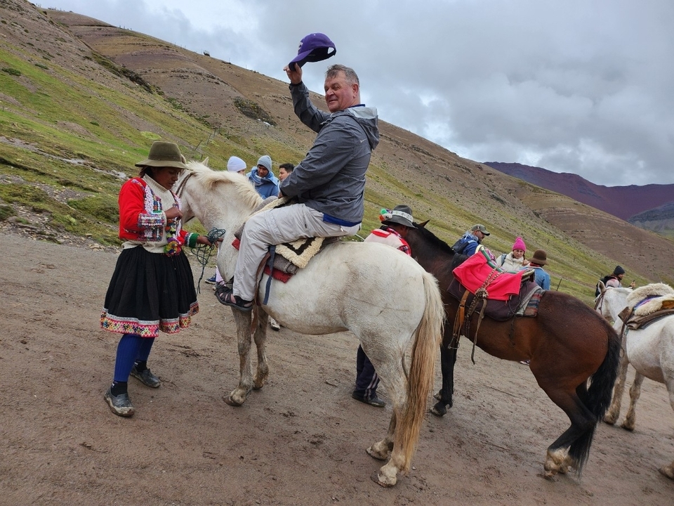 Un homme assis sur un cheval blanc mené par un local en tenue traditionnelle.