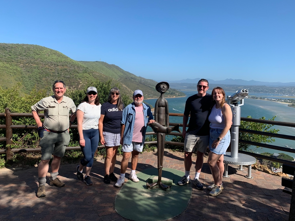 Group of people posing next to a statue overlooking a river.
