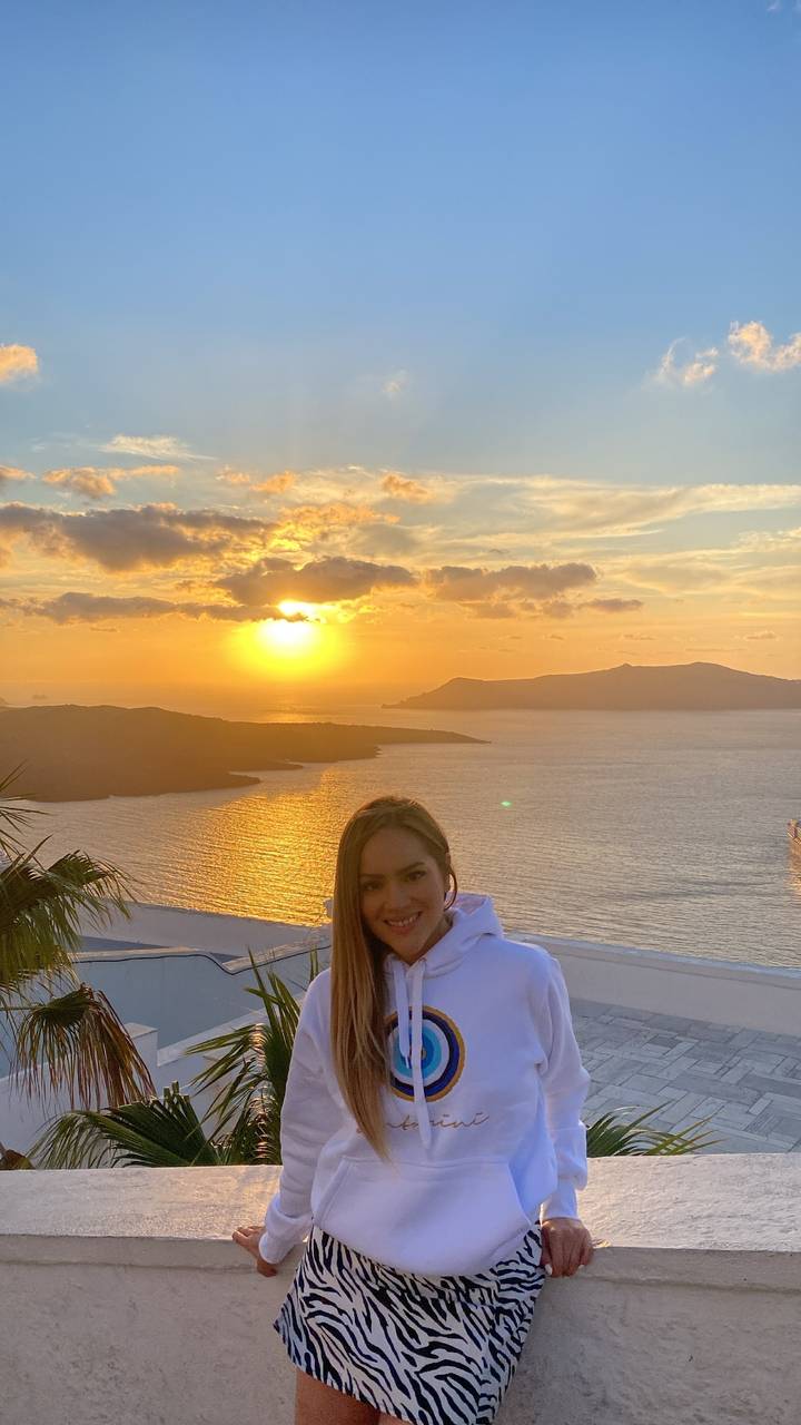 Woman smiling with a sunset over the sea in the background.