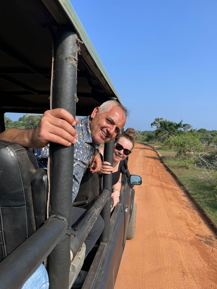 Deux personnes souriantes dans une jeep de safari sur un chemin de terre.