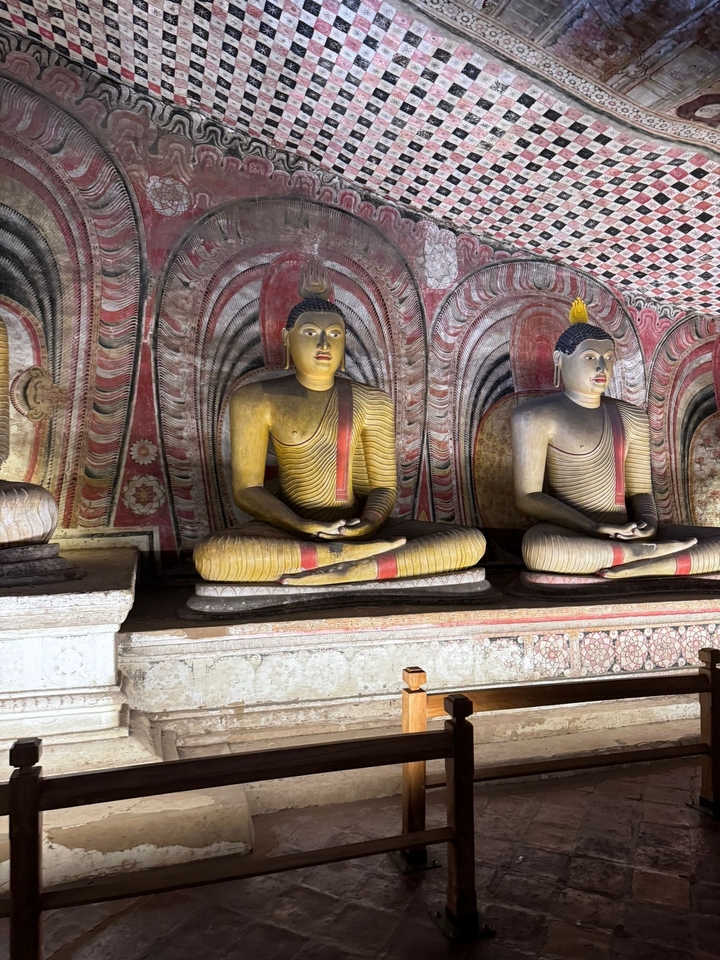 Statues de Bouddhas assis dans un temple avec des peintures murales détaillées.