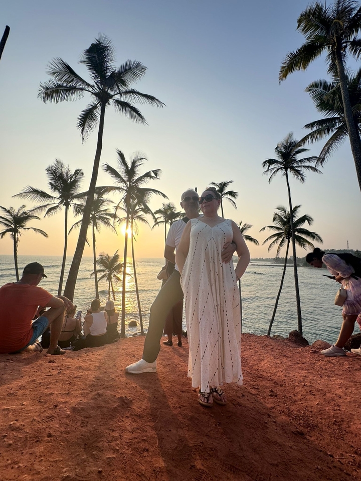 Couple posant sous les palmiers au coucher du soleil près de l'océan.