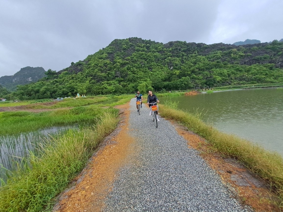 Deux personnes faisant du vélo sur un sentier le long d'un lac avec des montagnes en arrière-plan.