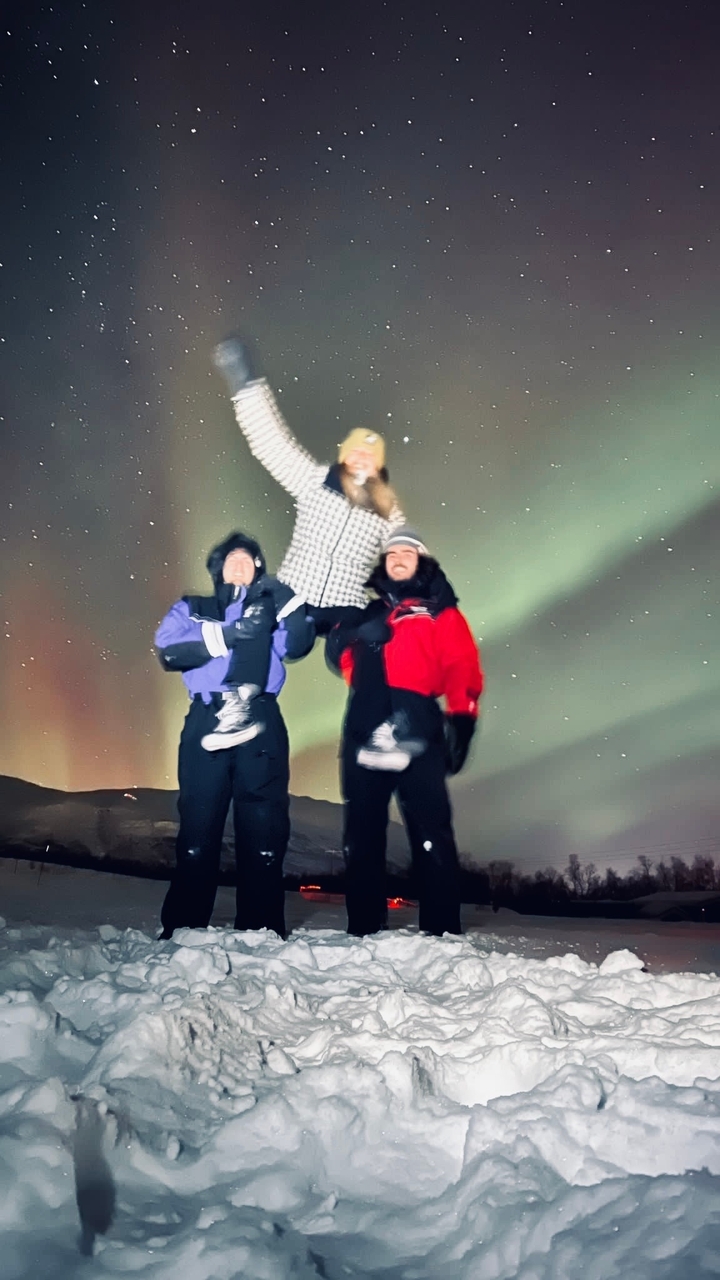Deux personnes soulevant quelqu'un sous l'aurore boréale.