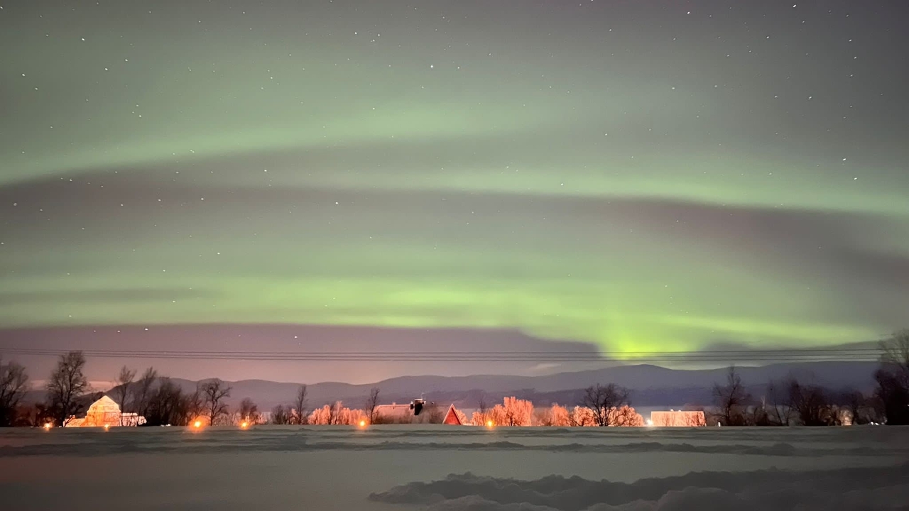 Aurores boréales au-dessus d'un paysage enneigé avec des chalets.