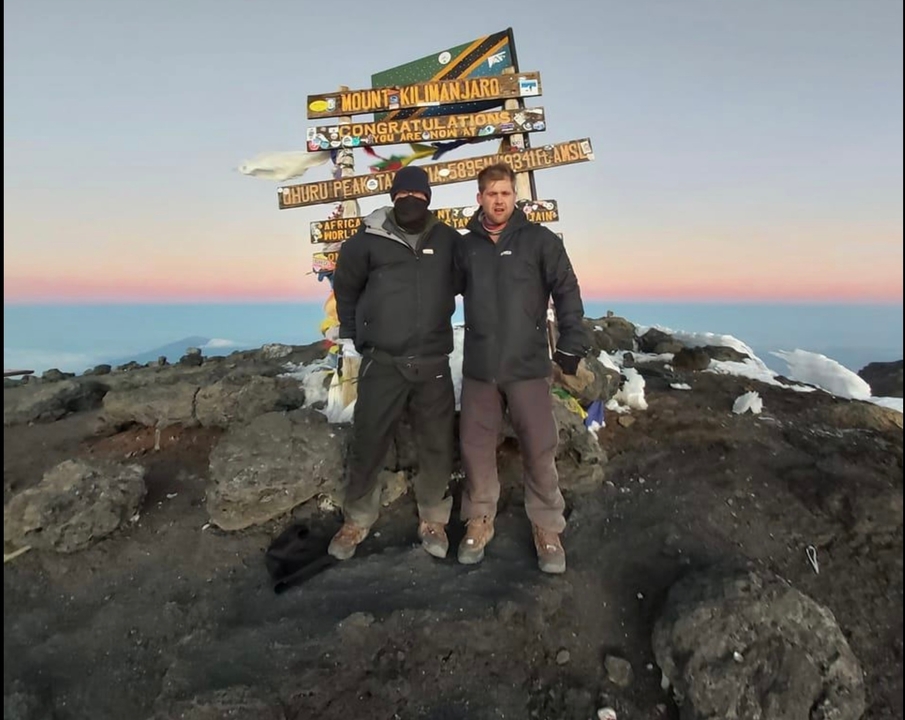 Deux personnes posant devant un panneau de sommet entourées d'un paysage rocheux.