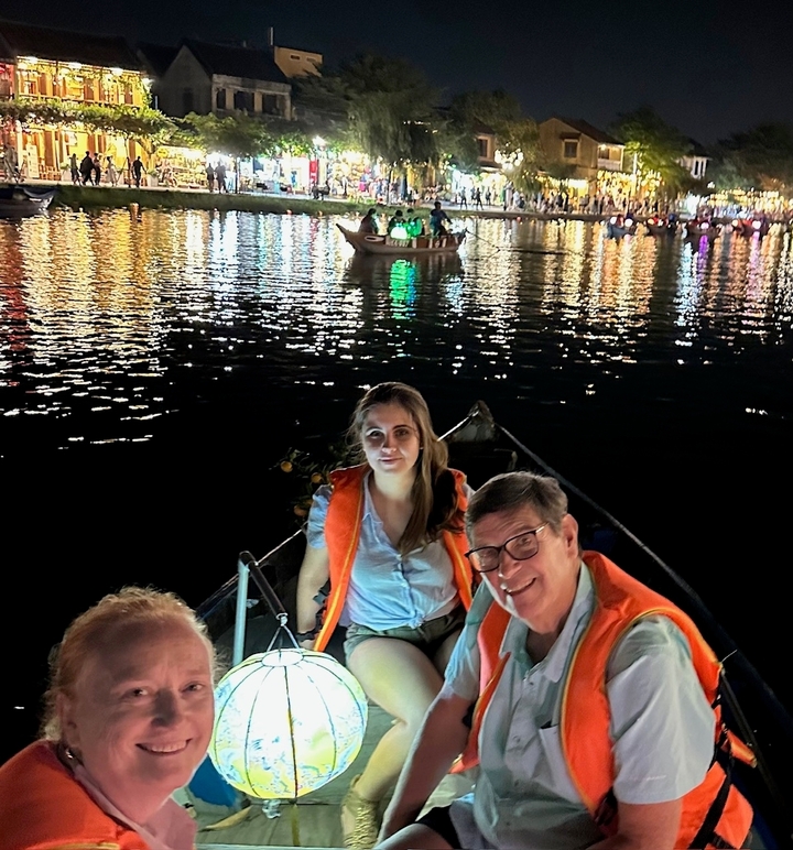 Des gens dans un bateau avec des lumières colorées qui se reflètent sur l'eau.