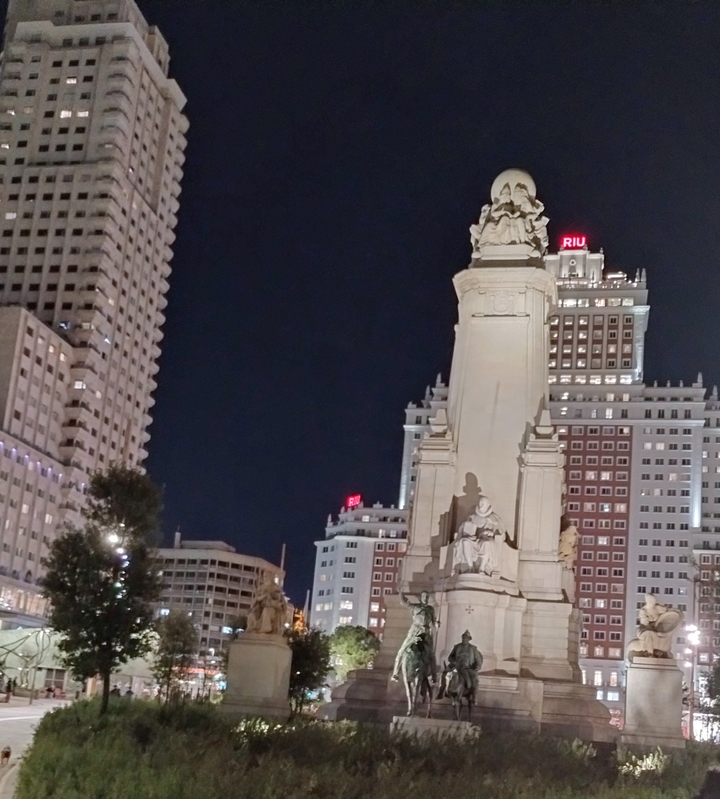 Statue devant des bâtiments illuminés la nuit.