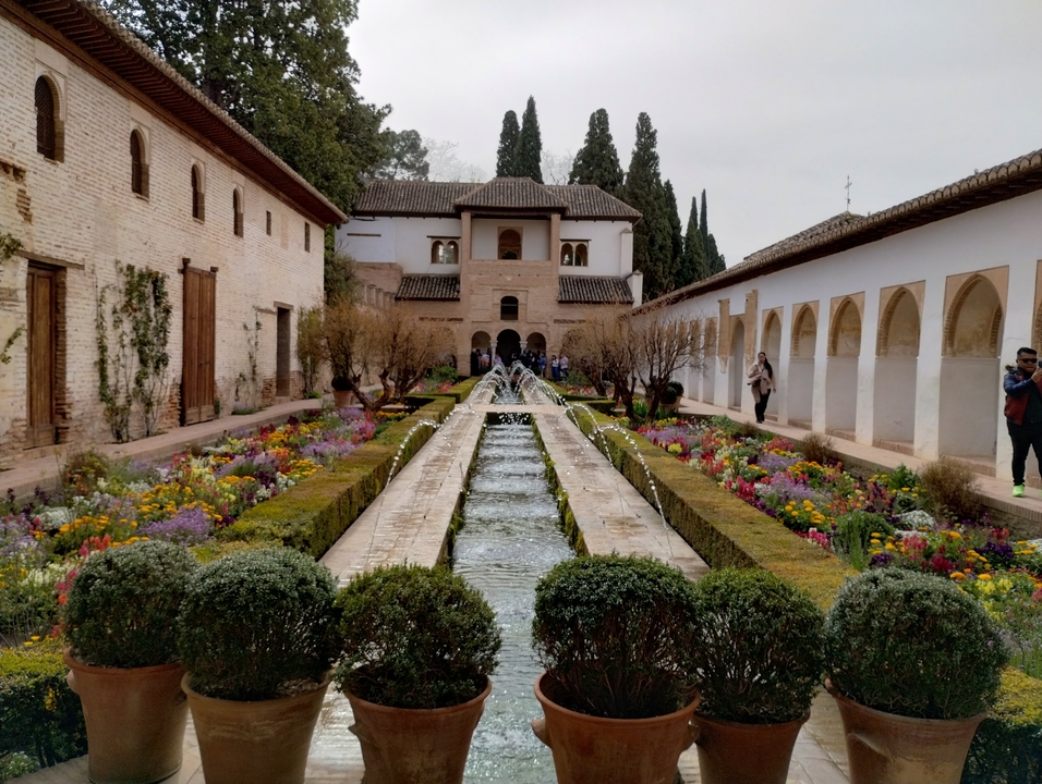 Jardins et fontaines avec un bâtiment historique, des gens se promènent.
