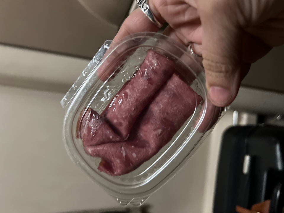 Hand holding plastic container with slices of processed meat in dim lighting