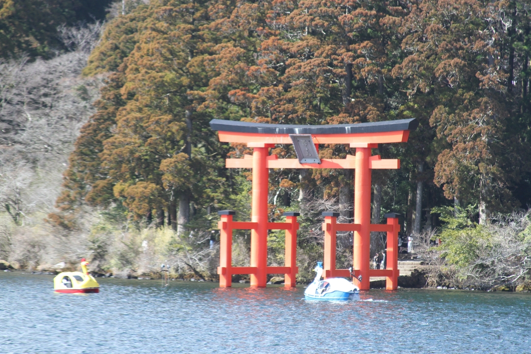 Torii rouge dans un lac avec des pédalos flottant à proximité.