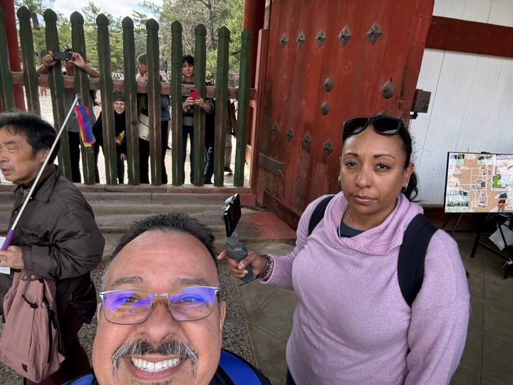 Deux personnes prenant un selfie devant un grand portail en bois.