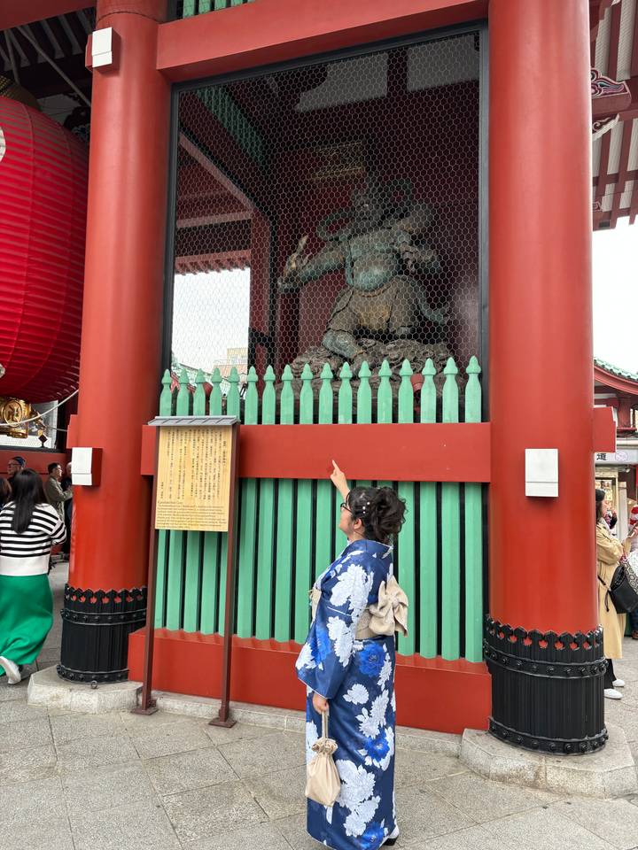 Personne en kimono pointant du doigt une statue derrière des barreaux.