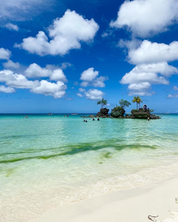 Belle plage avec une eau bleue claire et un petit îlot rocheux.