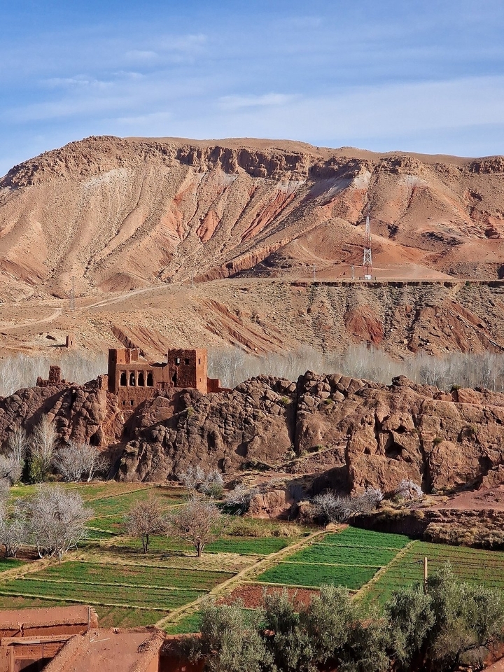 Ruines d'un château d'argile rouge sur un terrain rocheux.