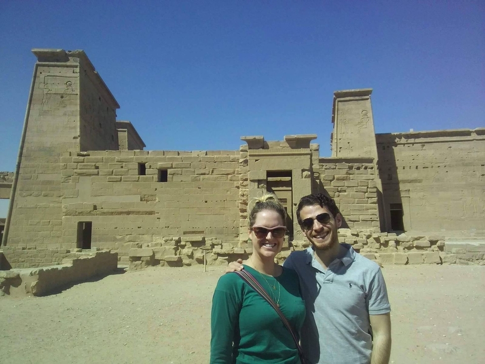 Un couple qui pose devant des ruines sous un ciel bleu dégagé.