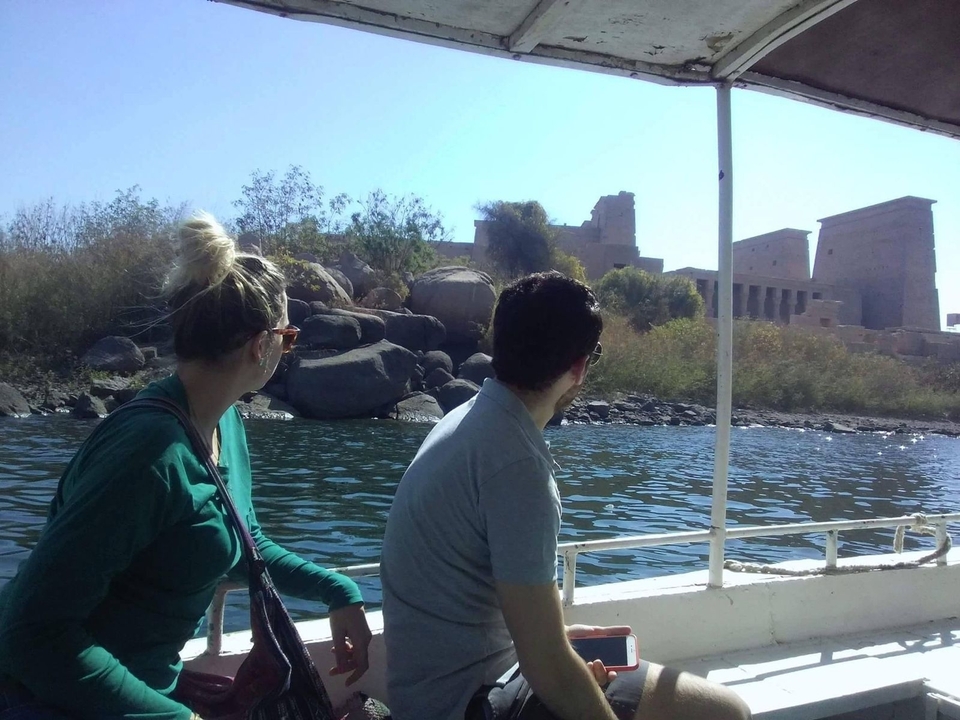 Un couple sur un bateau regardant des ruines au bord d'une rivière.