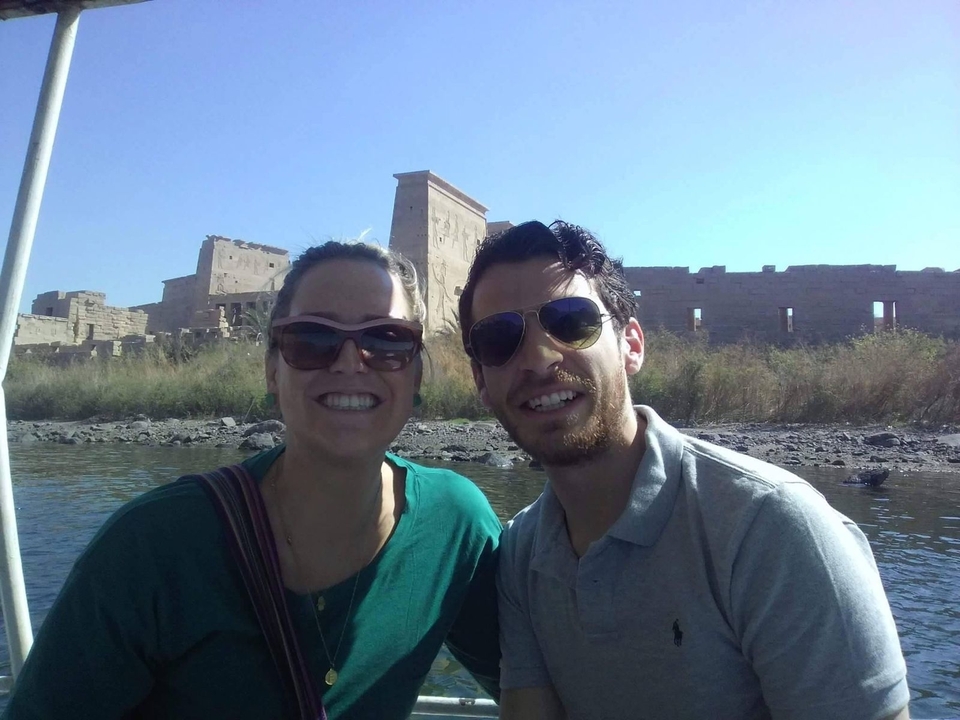 Un couple souriant sur un bateau avec des ruines en arrière-plan.