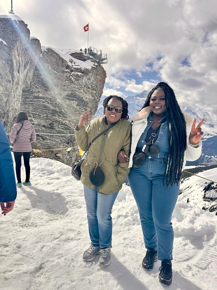 Deux personnes posant dans la neige avec des montagnes en arrière-plan.