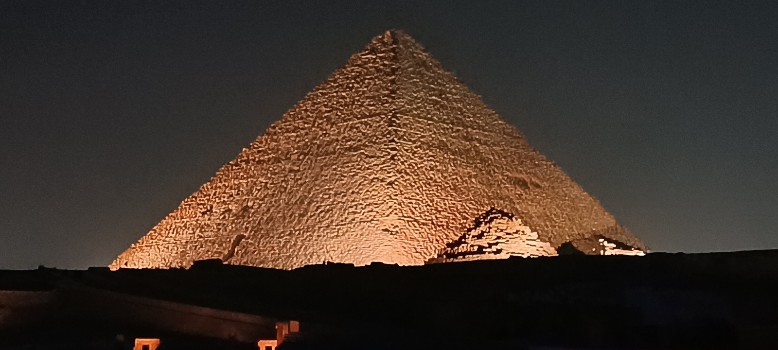 Pyramide illuminée pendant la nuit avec un ciel sombre.