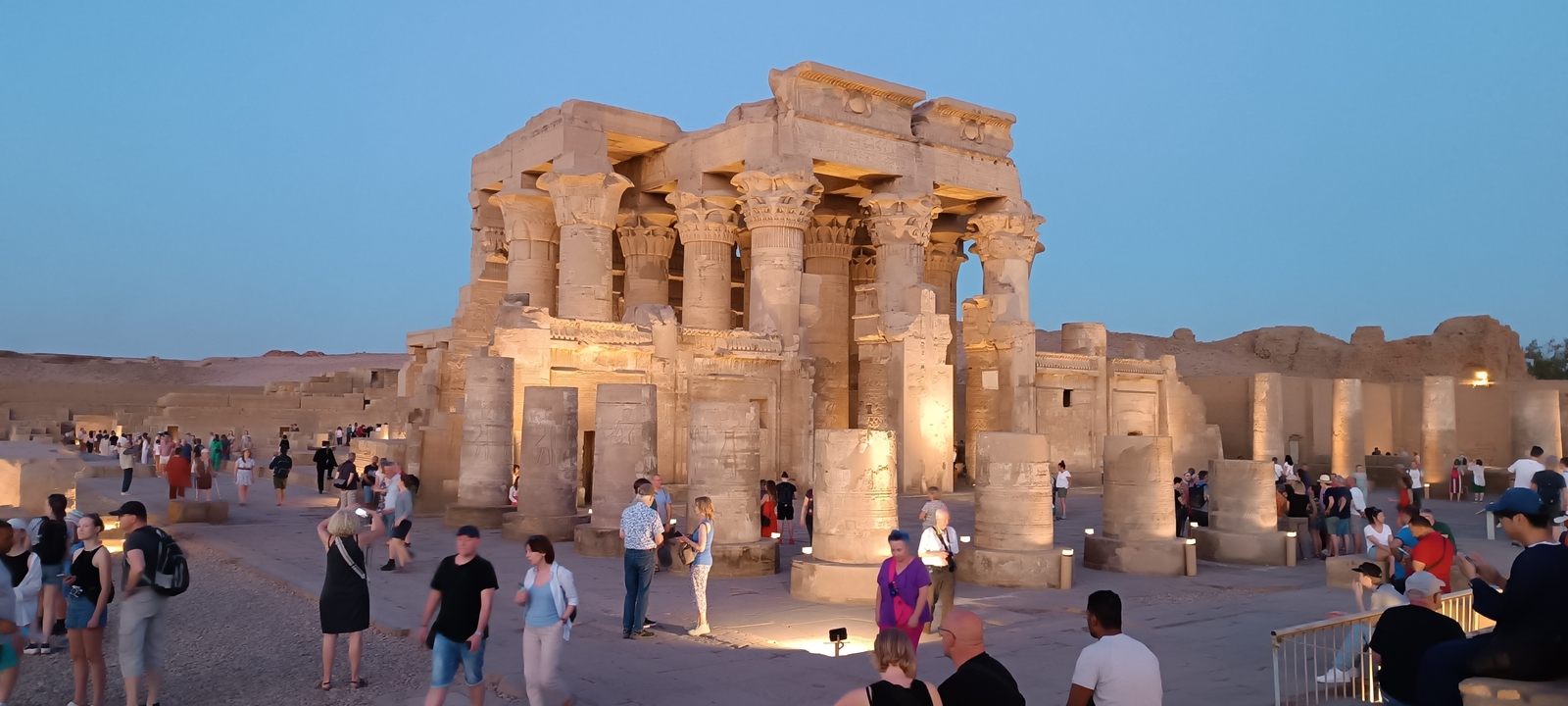 Ruines de temple avec colonnes, illuminées en début de soirée avec des touristes.